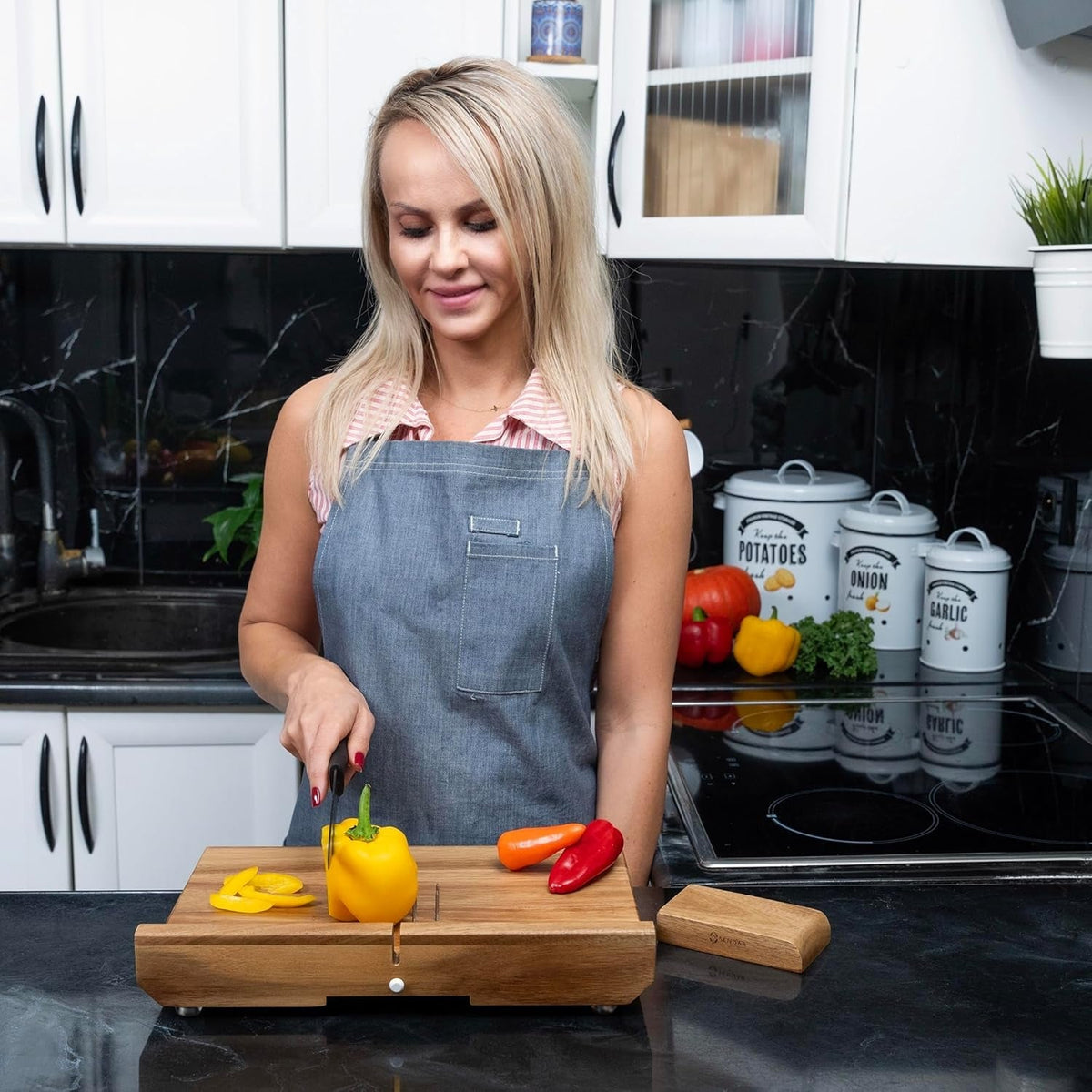 Person in a grey apron slicing a yellow bell pepper on a wooden cutting board.