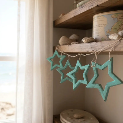 Close-up of weathered turquoise wooden star ornaments hanging on a rustic wooden shelf in a bright beachside cottage interior.