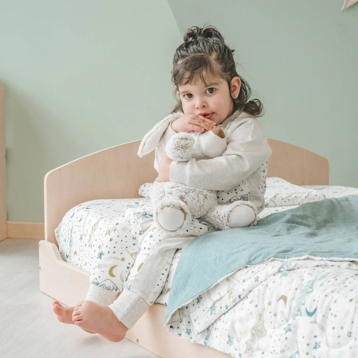 Cherry twin Montessori floor bed by Sapiens Child with a girl holding a stuffed animal in a cozy nursery setting.