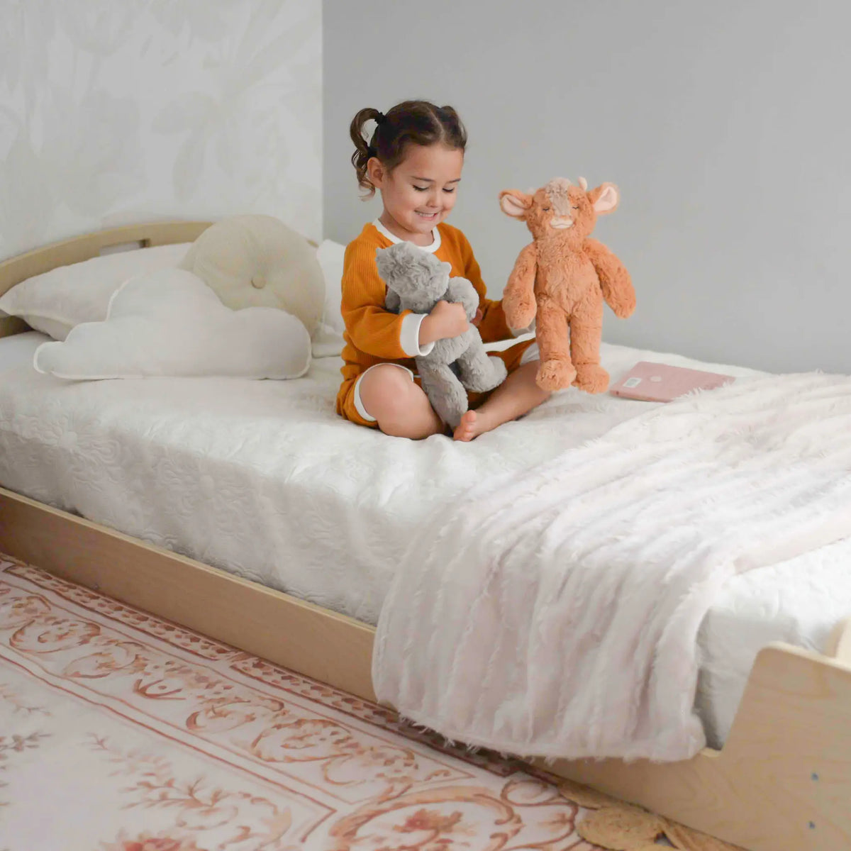 Sapiens Child cherry twin Montessori floor bed with built-in shelves for kids, featuring a sturdy wooden frame and colorful bedding.