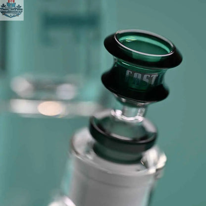 Castle Glassworks 14-inch teal beaker bong with colored logo and 9-hole downstem replacement, close-up on bowl and background.