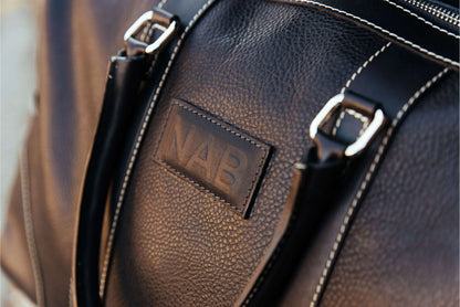 Black full-grain leather duffle bag by NAB Leather, featuring sturdy handles and a sleek design, made in Canada.