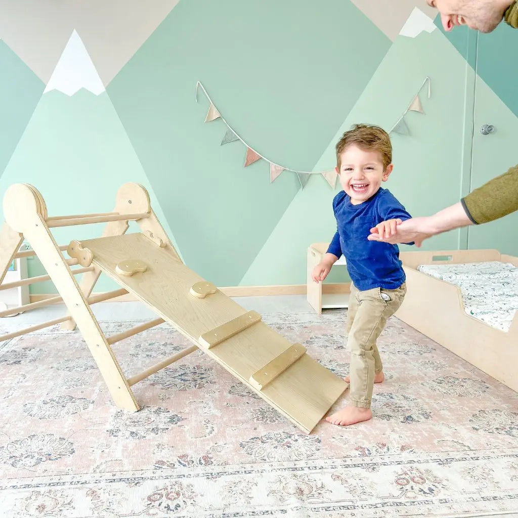 Smiling child holding dad's hand near Sapiens Child cranberry climber, Montessori wooden triangle climber for kids, happy and outdoors.