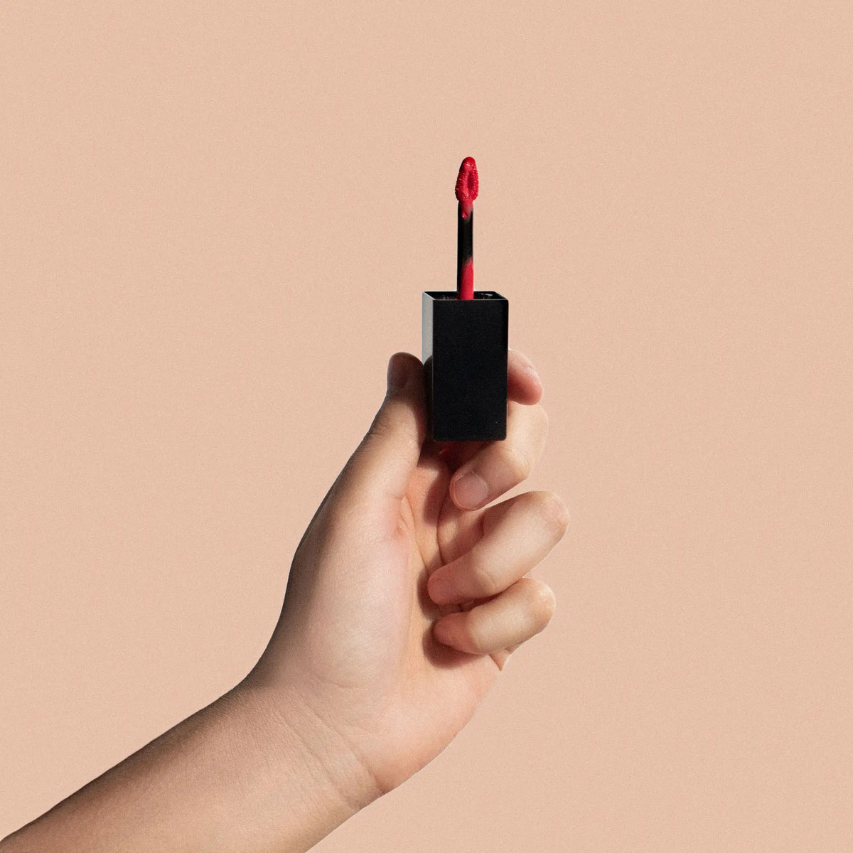 Vegan matte lipstick in True Crimson 77 by Fencygrace, shown in a sleek lipstick tube with vibrant red color.