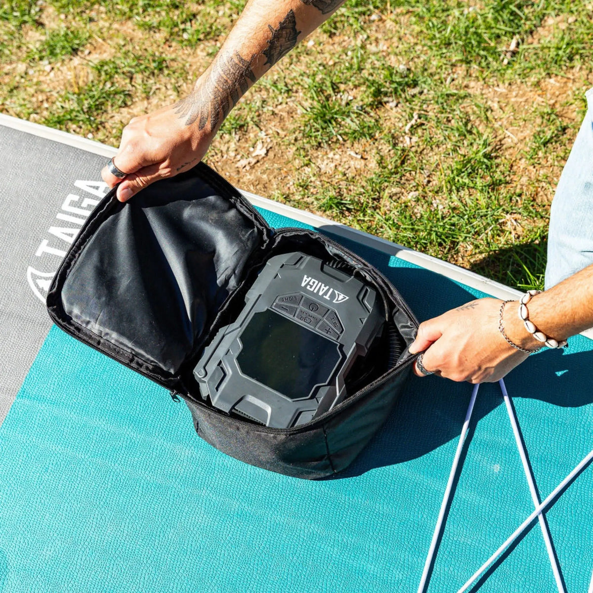Taiga Board premium electric pump for paddle boards, showing the battery-operated inflator with control panel and hose attached.